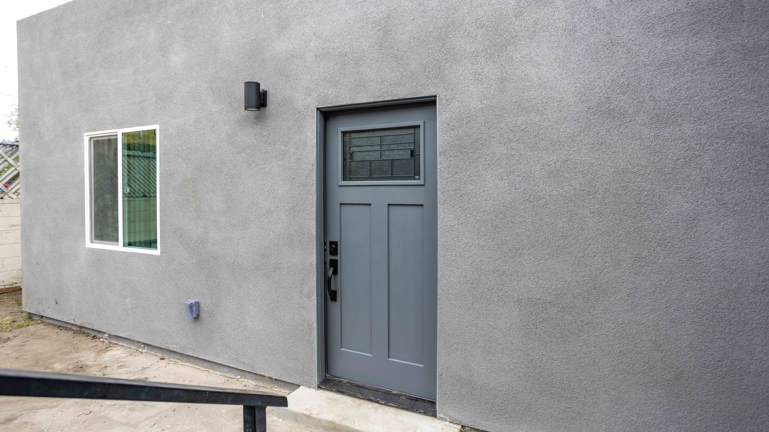 Completed garage-to-ADU conversion with a new entry door and window set where the vehicle opening was, finished in continuous stucco