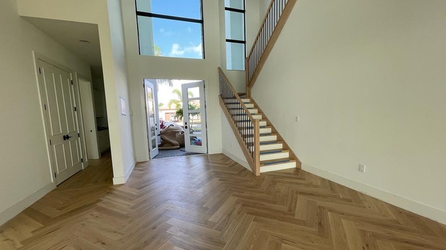 Light oak herringbone wood flooring running through a double-height living space in a completed South Florida home