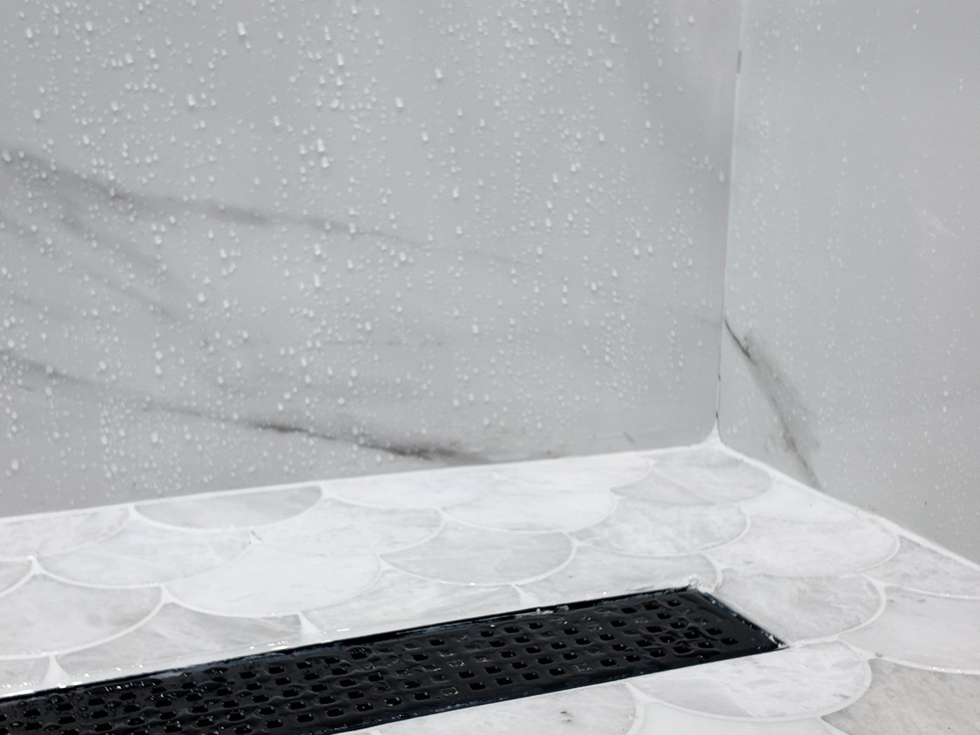 Matt black linear drain grate set into a scalloped mosaic shower floor