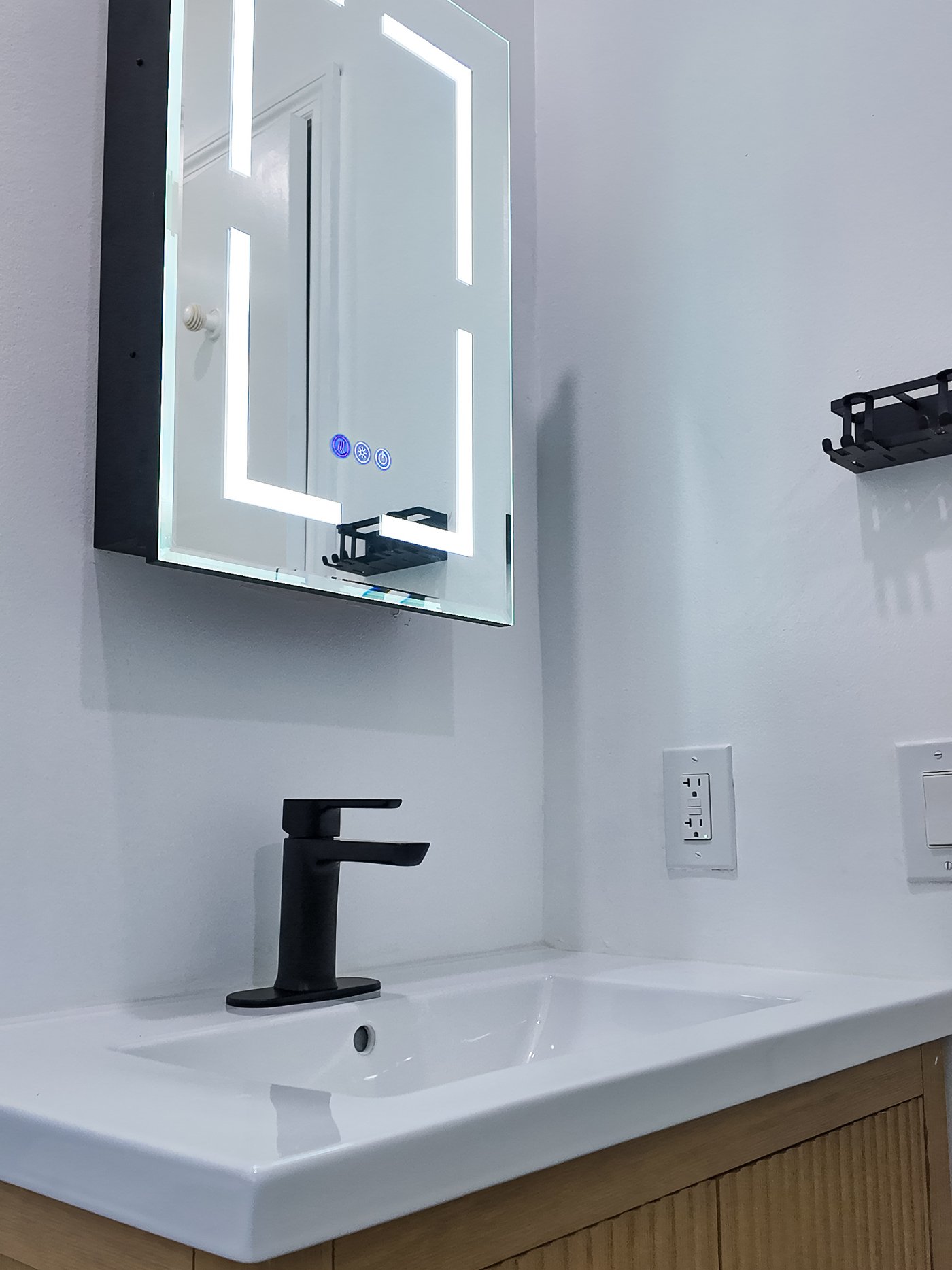Backlit LED mirror cabinet above a vanity with matt black fittings