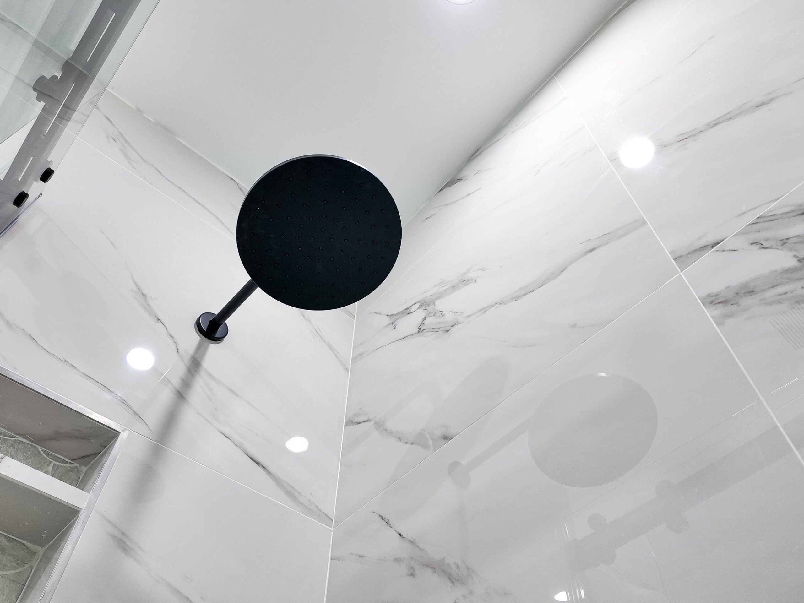 Ceiling-fed matt black shower head against a large-format porcelain wall