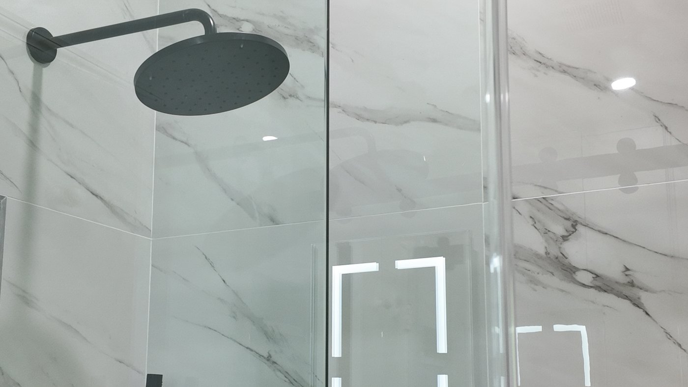 Completed walk-in shower with full-height marble-look porcelain, a scalloped mosaic floor, a linear drain and matt black fixtures