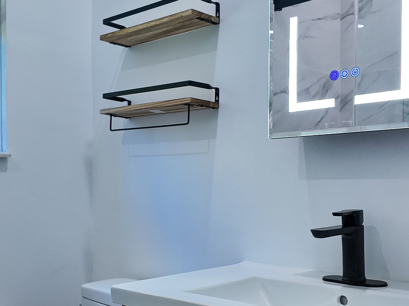 Fluted light oak vanity with a white top, black handles and a backlit mirror cabinet above